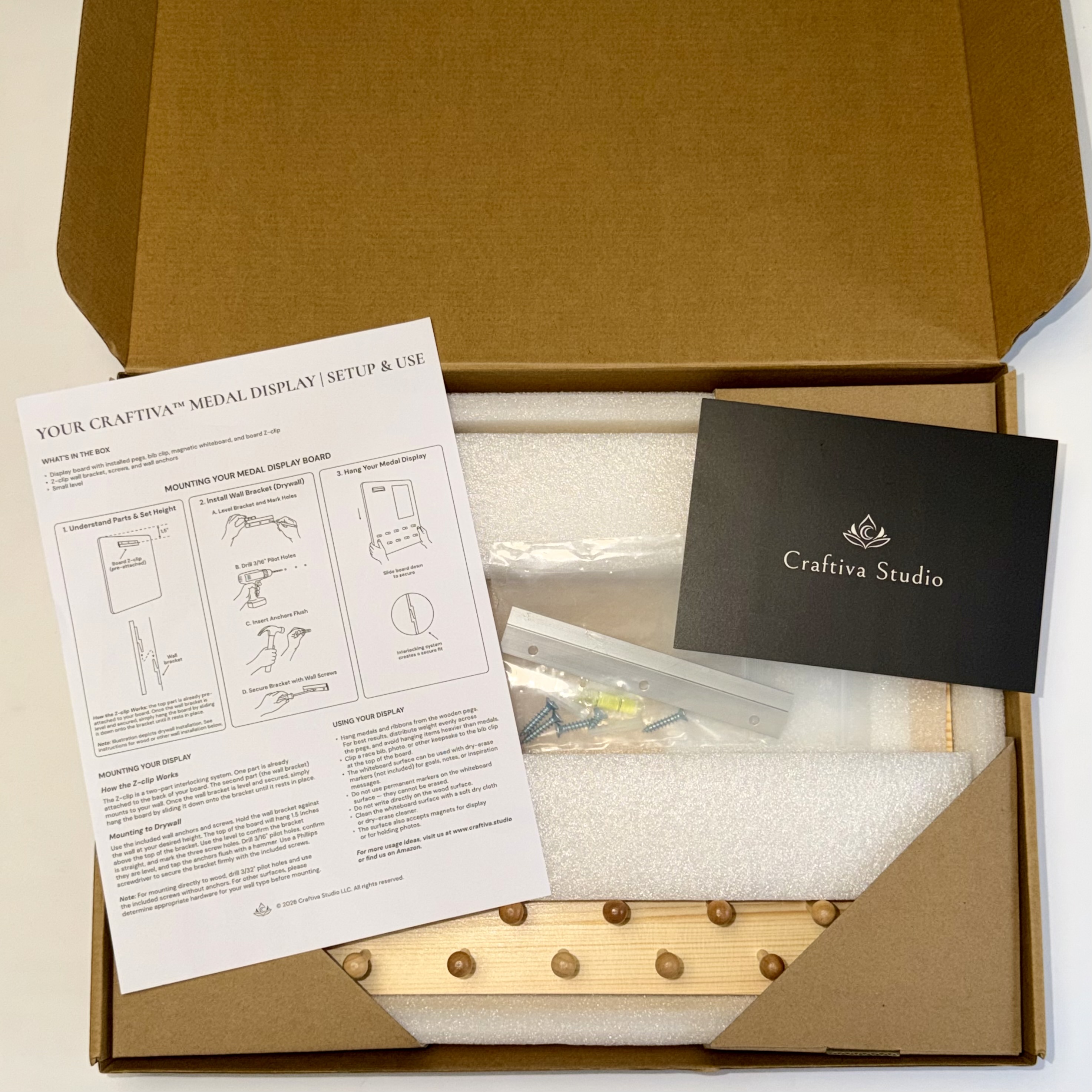 Open Craftiva medal display package with protective foam, mounting hardware, instructions, and printed card