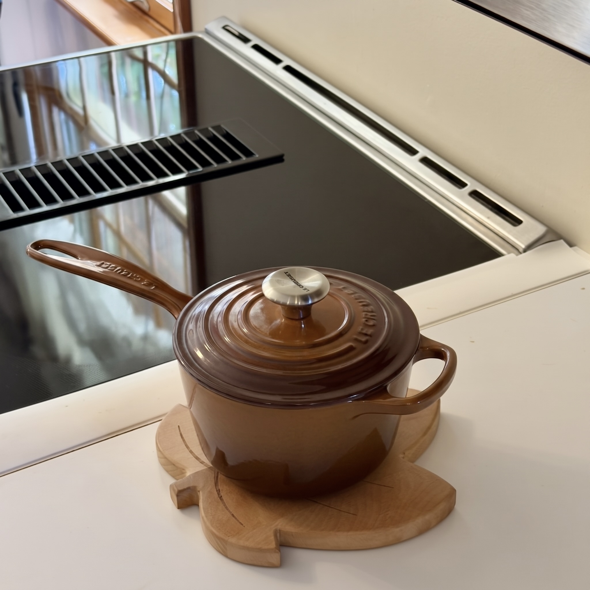 Brown saucepan resting on the leaf trivet beside a stovetop