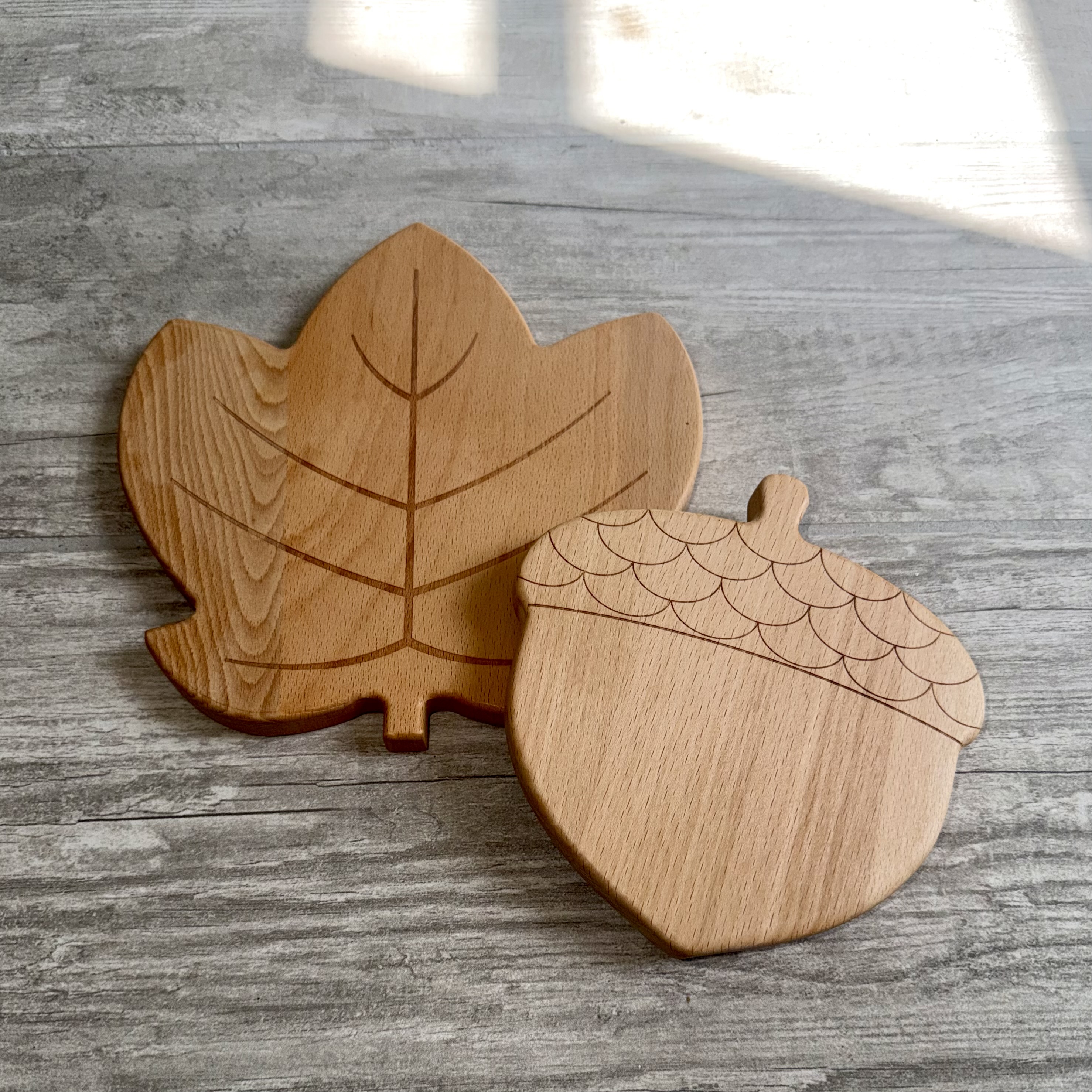 Leaf and acorn trivets showing their carved patterns and solid beech grain